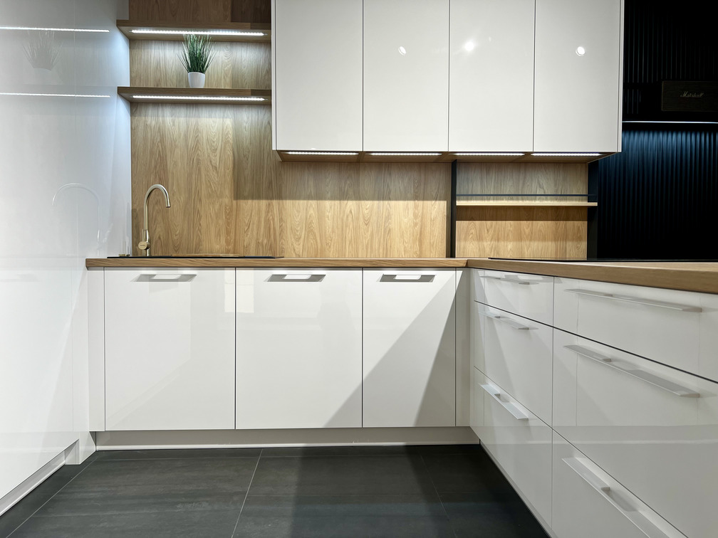 Kuchyňa vyrobená na mieru v modernom štýle – prevažne biele, vysokolesklé skrinky bez úchytiek sú zjemnené vodorovnými pásmi prírodného dubu Hickory.