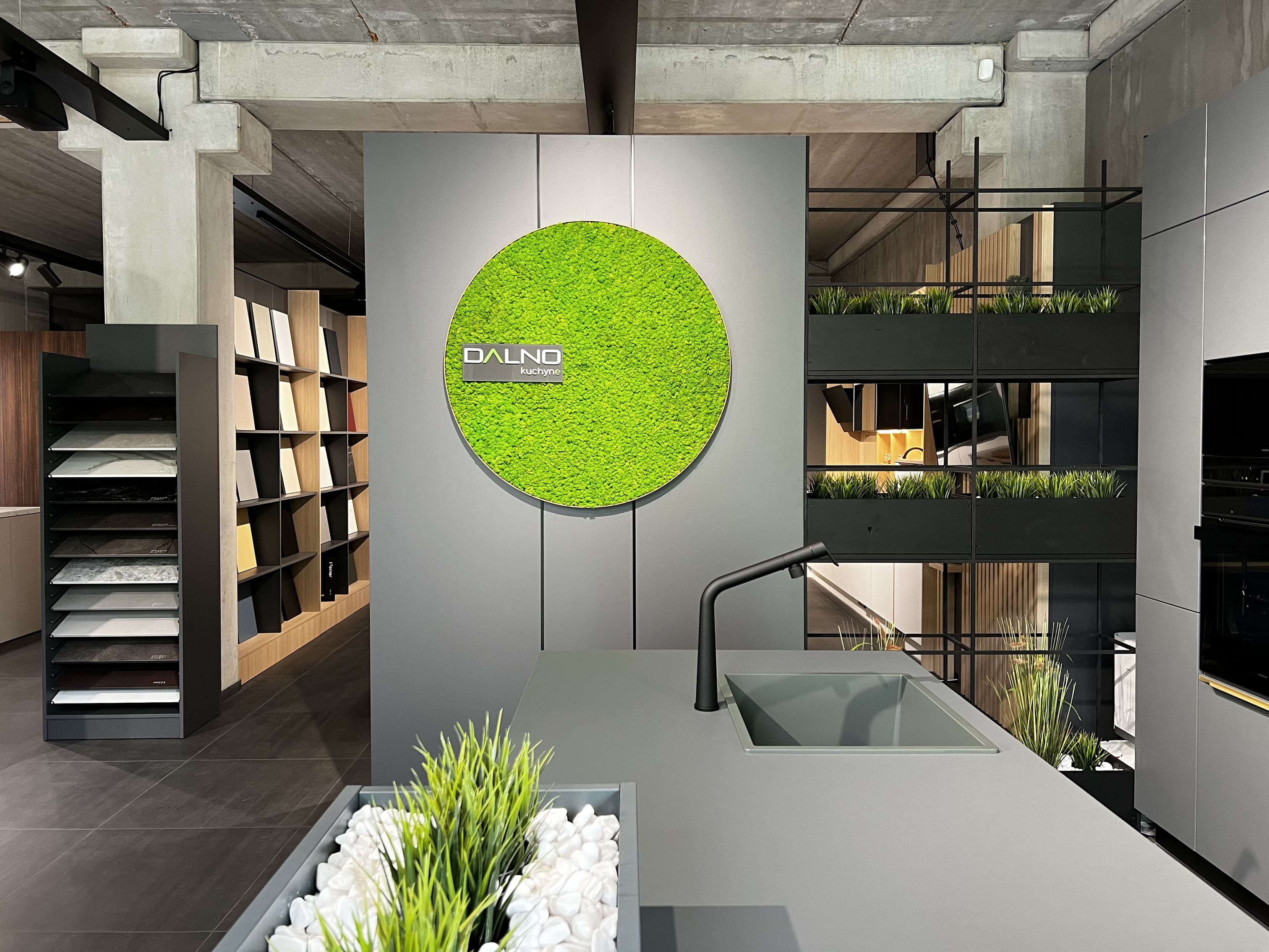 Detail spodných skriniek s povrchom NANOTEQ v hlbokej petrolejovo‑zelenej – ultra‑matná, zamatovo hebká nanoúprava pohlcuje odlesky, minimalizuje odtlačky prstov a zvyšuje odolnosť voči mikroškrabancom; do čistých plôch sú zapustené dlhé mosadzné lištové úchytky, ktoré zvýrazňujú horizontálnu líniu kuchyne, nad jemnosivou pracovnou doskou sa tiahne biely mramorový obklad a horné skrinky z dubovej dyhy dodávajú teplý kontrast.