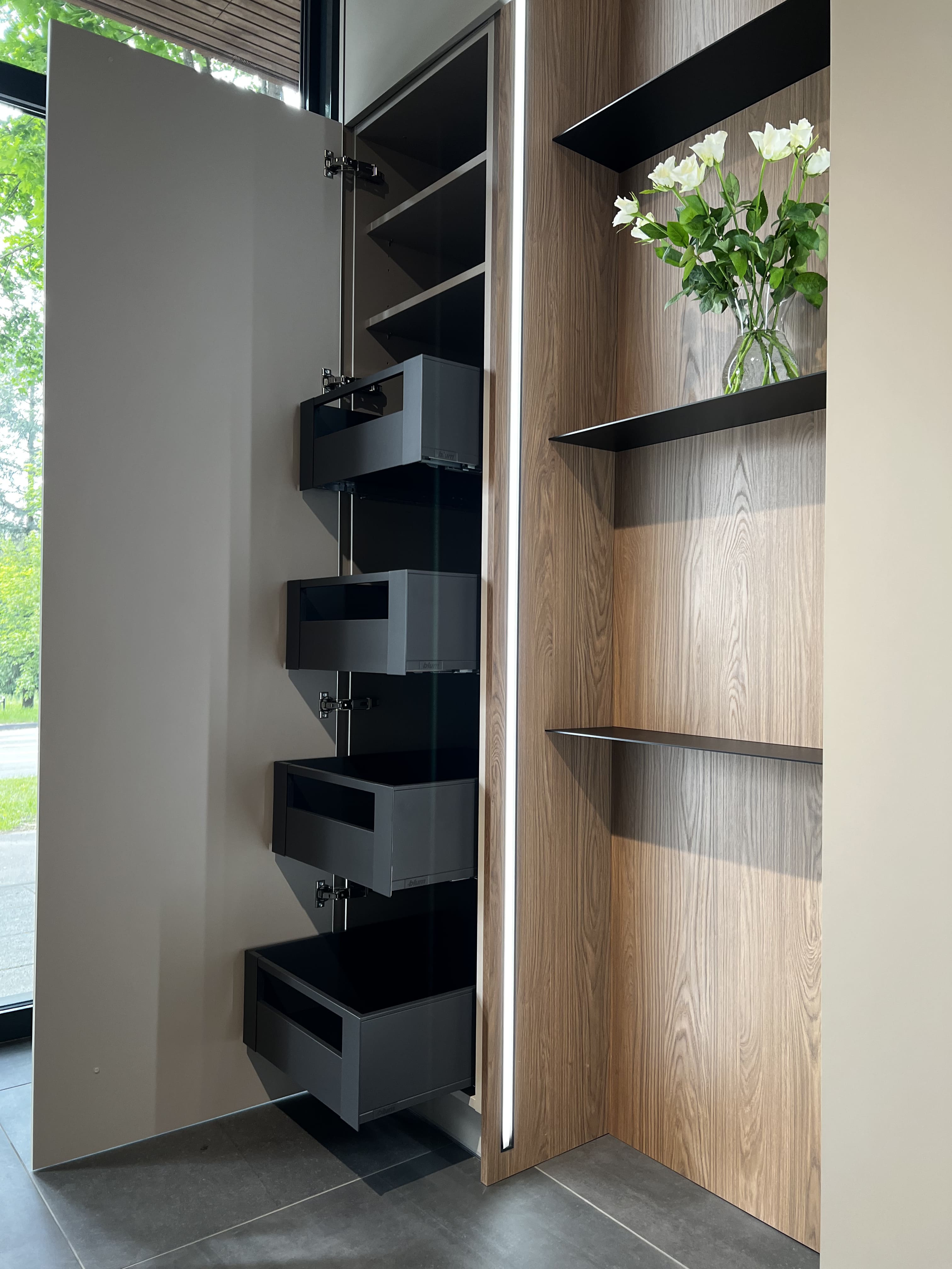 Otvorený pohľad do vnútorného vybavenia kuchyne – zásuvky a výsuvné koše s antracitovými kovovými bokmi a tlmeným dovieraním, organizéry na príbory a korenie v teplom dekore dub Casella hnedý, spodné police s protišmykovými rohožami v povrchu kamenná sivá matt a integrované LED pásy osvetľujú obsah; precízne rozdelené priehradky umožňujú prehľadné uloženie riadu, potravín aj kuchynského náradia.